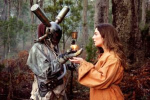 A woman in a costume offers an apple to a man in a costume, both engaged in a playful exchange.