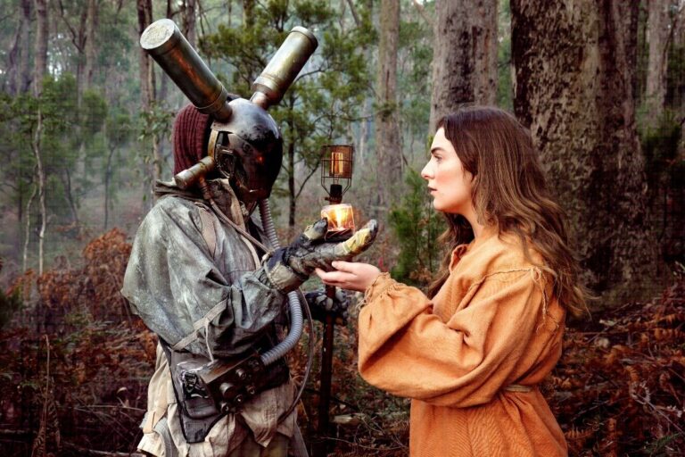 A woman in a costume offers an apple to a man in a costume, both engaged in a playful exchange.