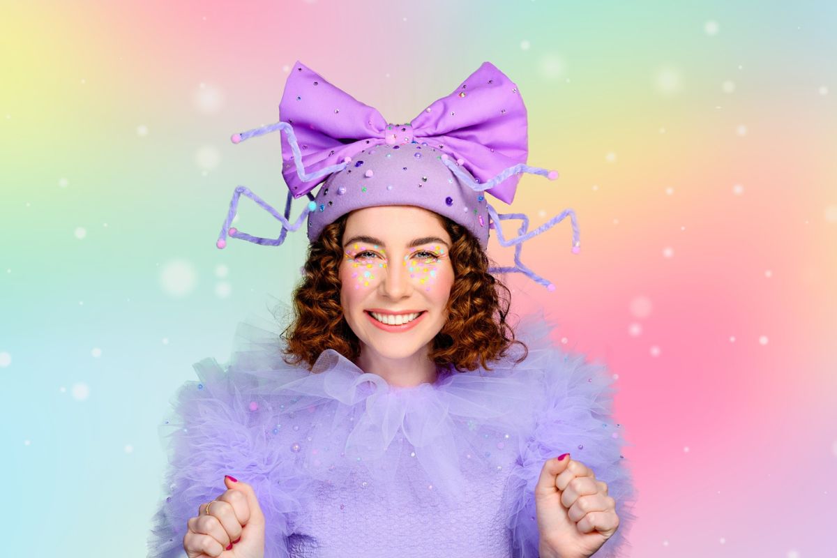 A woman wearing a purple dress and matching purple hat stands elegantly, showcasing her stylish outfit.