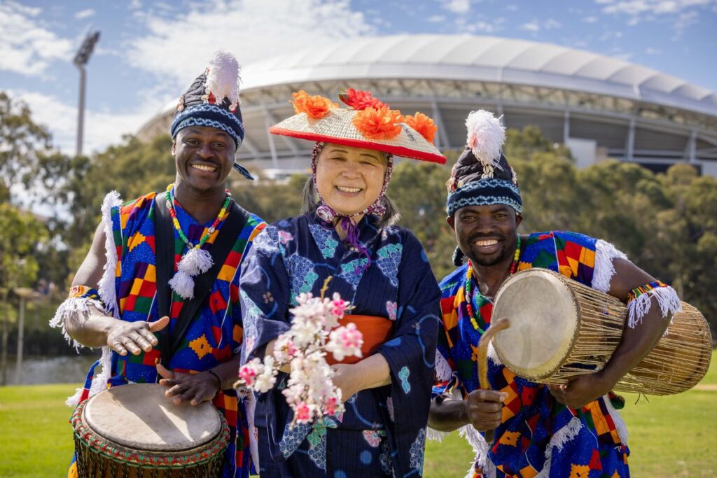 A group of three people dressed in traditional clothing smiles for a photo, highlighting their cultural attire and unity.