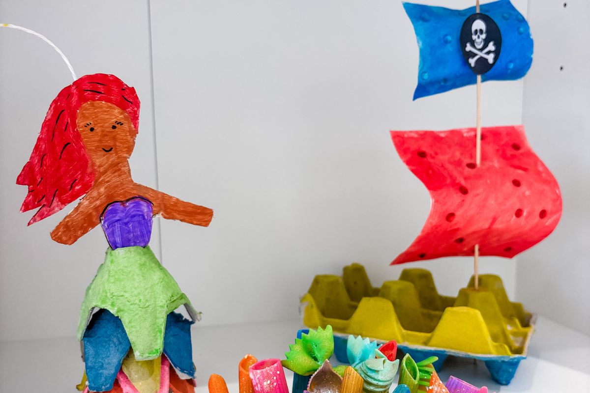 A delicate paper boat alongside a whimsical mermaid, both showcased in an artistic display.