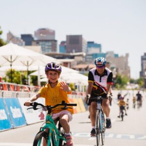 A young girl riding a bicycle on a city street, surrounded by buildings and trees.