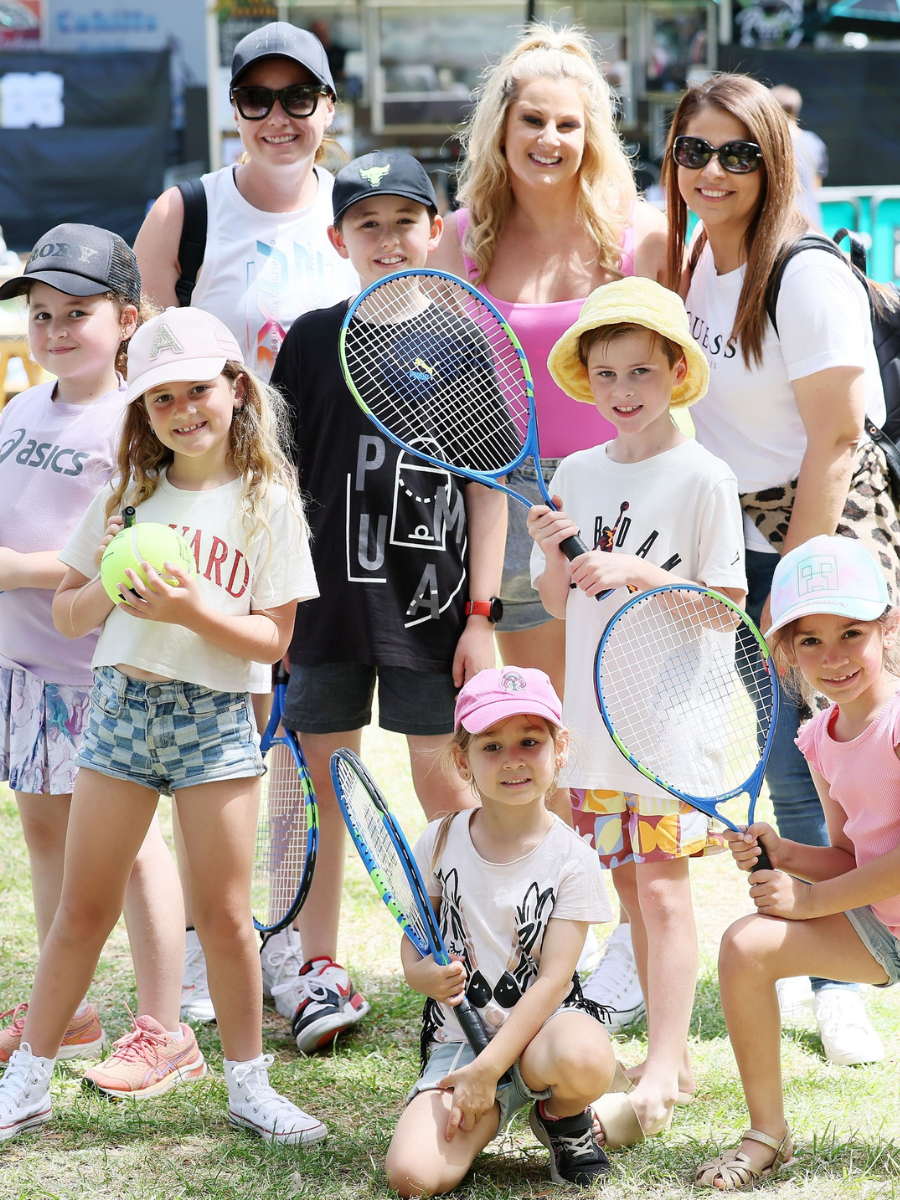 A group of children and adults smiling and posing together for a tennis photo outdoors.