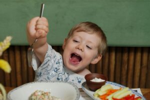 A child enthusiastically enjoys their meal in a cafe setting