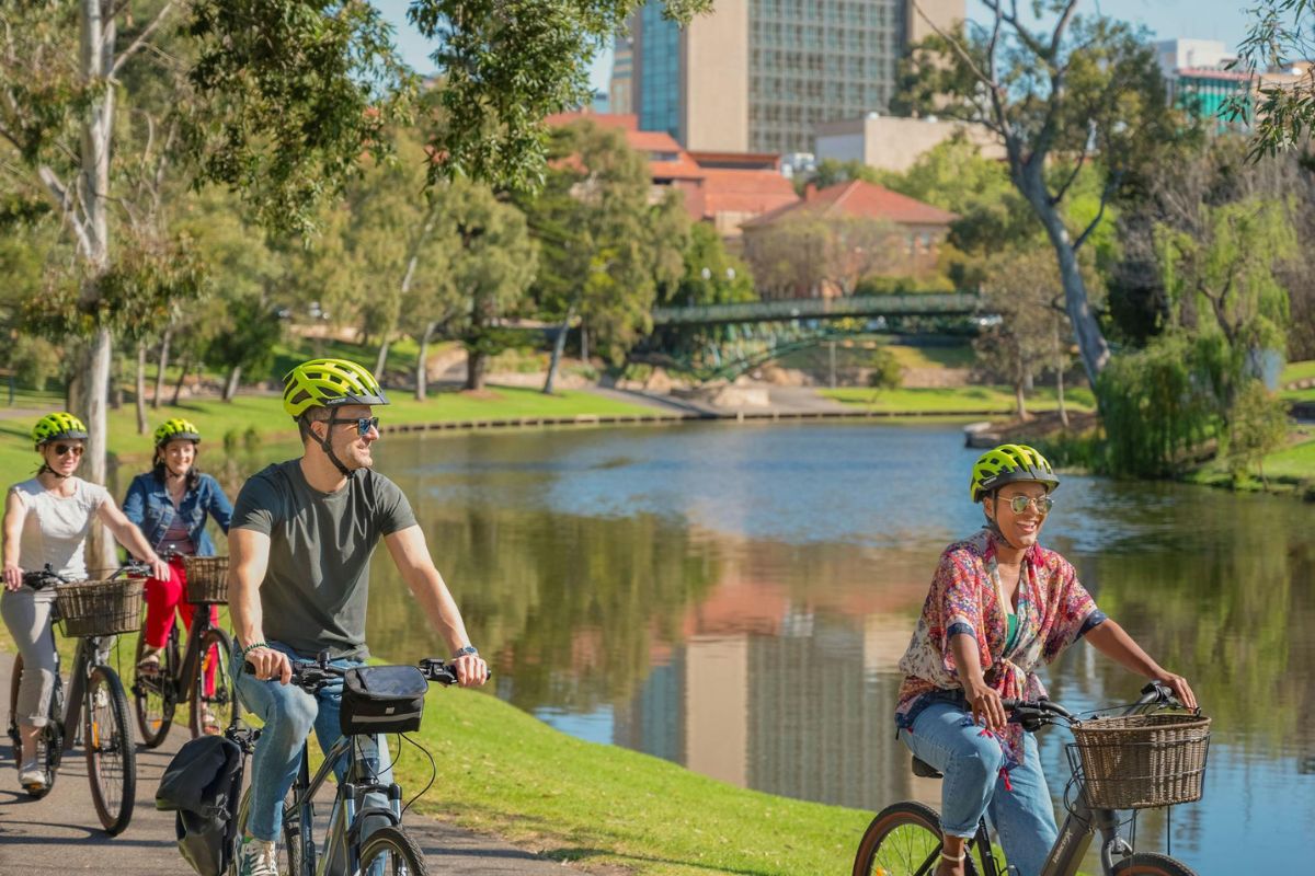 A group of people cycling along a river, enjoying the scenic view and fresh air on a sunny day.