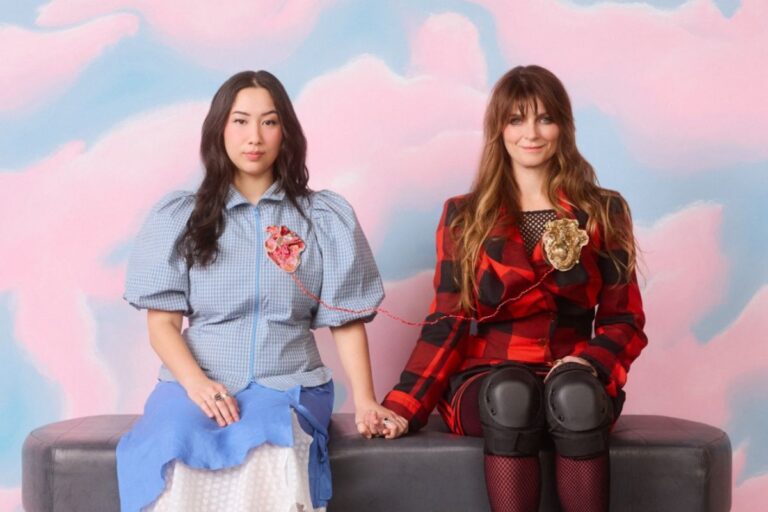 Two women with roller skates sit on a bench, engaged in conversation and laughter in a vibrant environment.