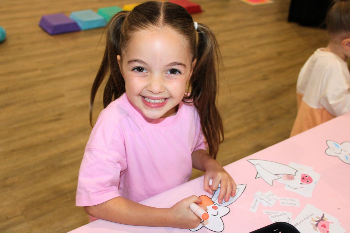 A young girl in pig tails smiles at the camera while enjoying drawing