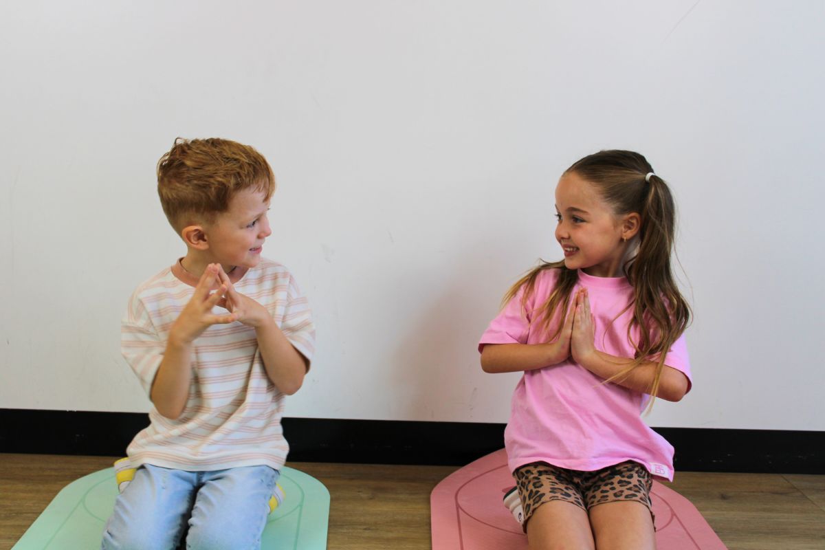 A young boy and girl practice yoga kneeling on mats in a gymnasium 