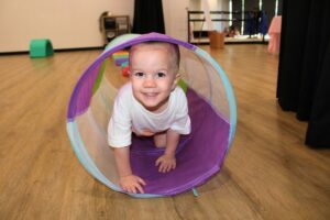 A toddler laughs while crawling through a colourful tube