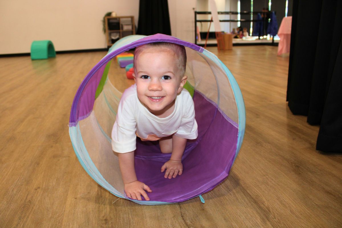 A toddler laughs while crawling through a colourful tube