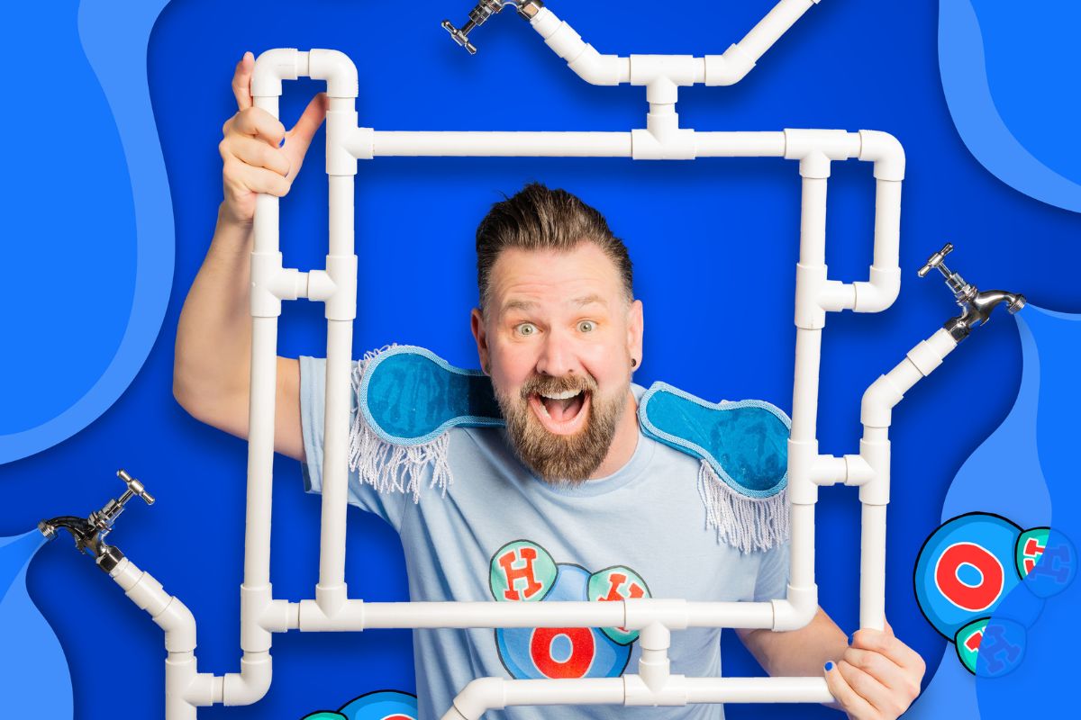 A man poses energetically with a frame of plumbing pipes and taps framing his face