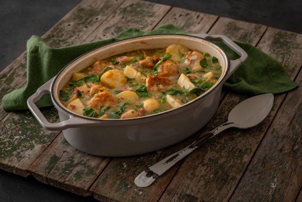 A white dutch oven casserole dish on a wooden table with enamel spoon in a rustic setting for a wholesome meal