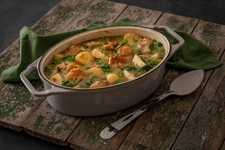 A white dutch oven casserole dish on a wooden table with enamel spoon in a rustic setting for a wholesome meal