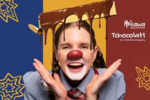 A woman dressed as clown with a red clown nose and chocolate poured on her head smiles in surprise