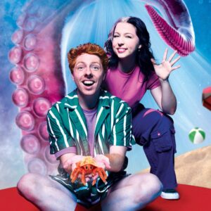 A man holds a small sea creature posing with a friendly waving woman in an under the sea staged setting