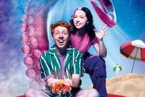 A man holds a small sea creature posing with a friendly waving woman in an under the sea staged setting