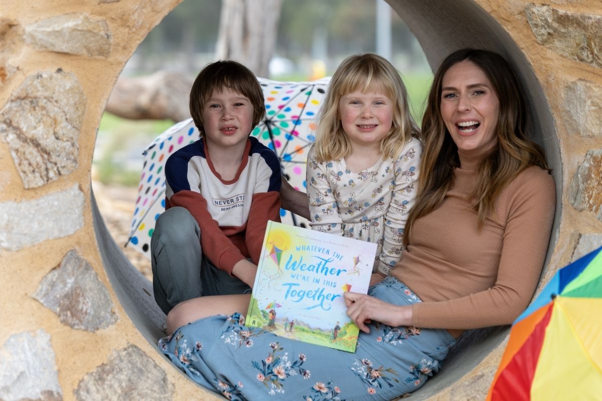 A woman and two children sit together in a tunnel, reading a book, surrounded by the tunnel's curved walls.