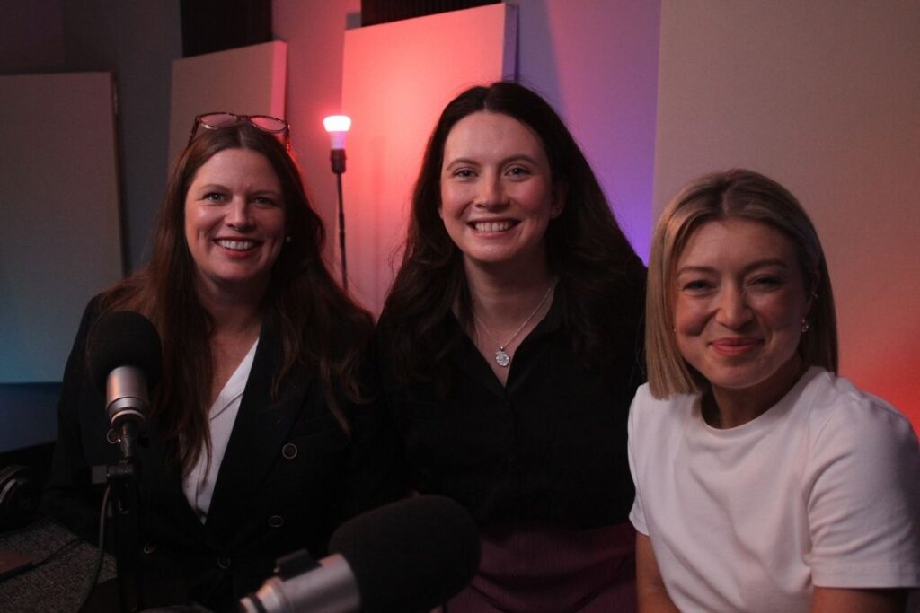 Three women smile brightly in front of a microphone, showcasing a moment of happiness and connection.