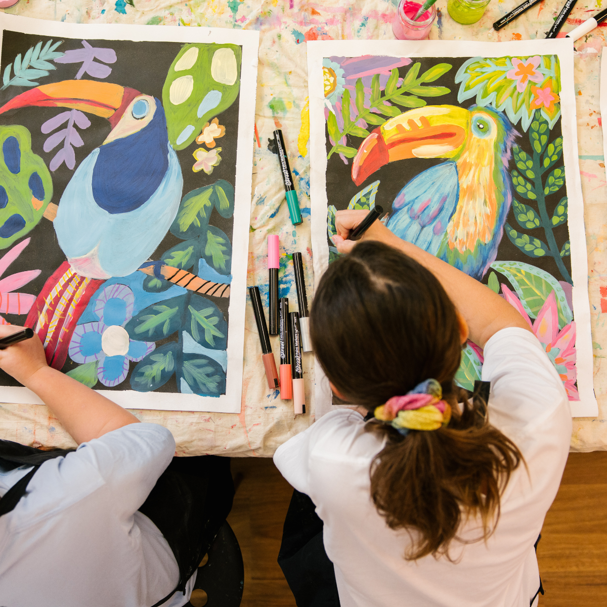 Two children are engaged in painting on canvases, surrounded by colorful art supplies and a bright, cheerful environment.