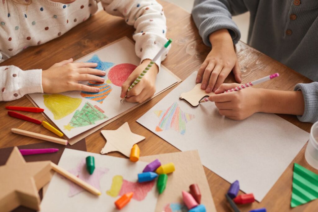 Young children participating in arts and crafts with colourful materials around a small table in an art class.
