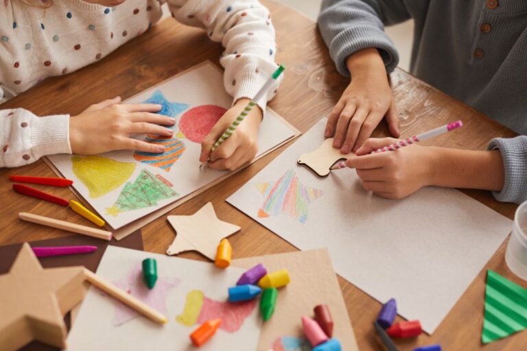 Young children participating in arts and crafts with colourful materials around a small table in an art class.