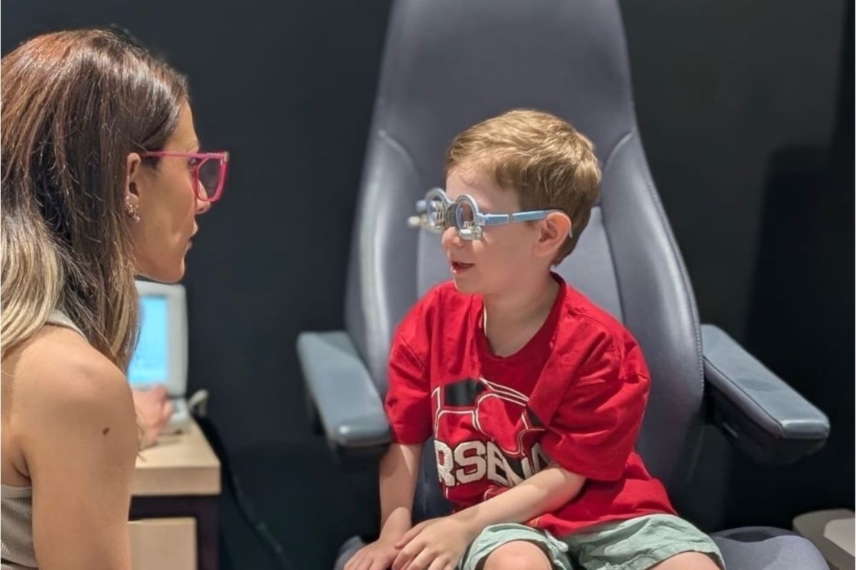 A woman converses with a boy seated in a chair, engaging in an eye examination