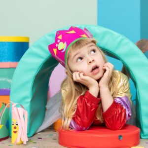 A girl dressed in a birthday crown looks up in amazement in a colourful room. 