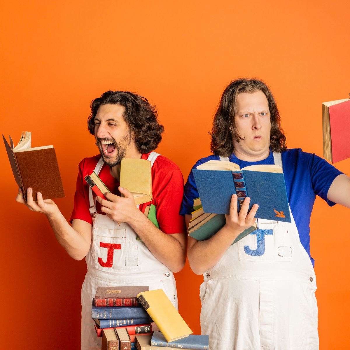 Two people in overalls making playful faces while reading books.