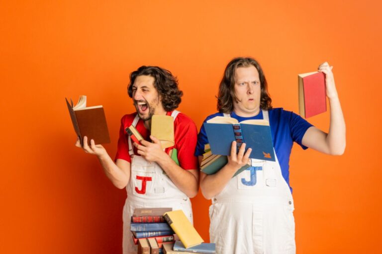 Two people in overalls making playful faces while reading books.