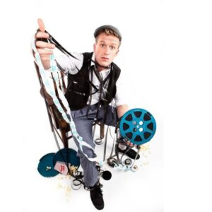 A man holds a pulled reel of camera film with a face of dismay in the chaos.