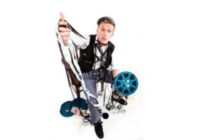 A man holds a pulled reel of camera film with a face of dismay in the chaos.