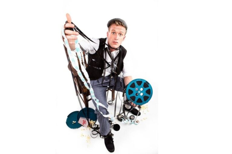 A man holds a pulled reel of camera film with a face of dismay in the chaos.