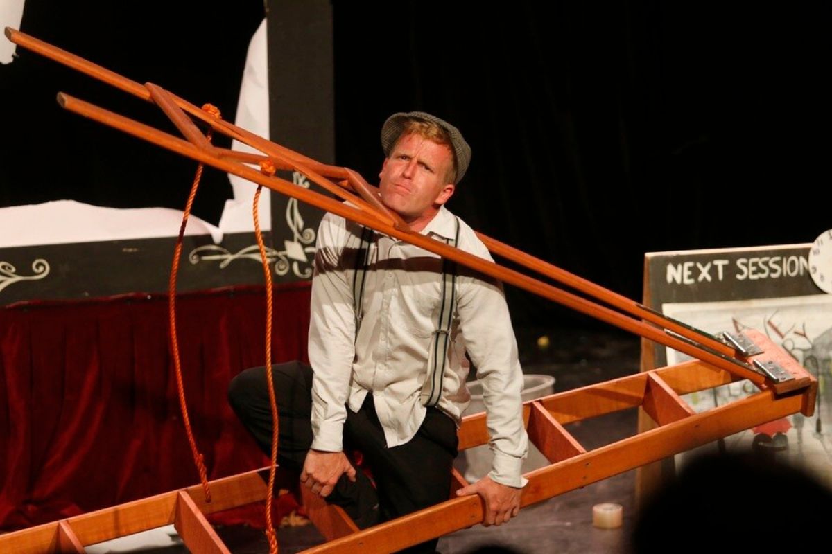 A man grips a wooden ladder while performing, showcasing his focus and balance in the activity.