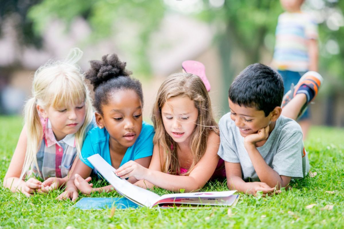 Four children lay on grass reading a book enthralled by the pages.