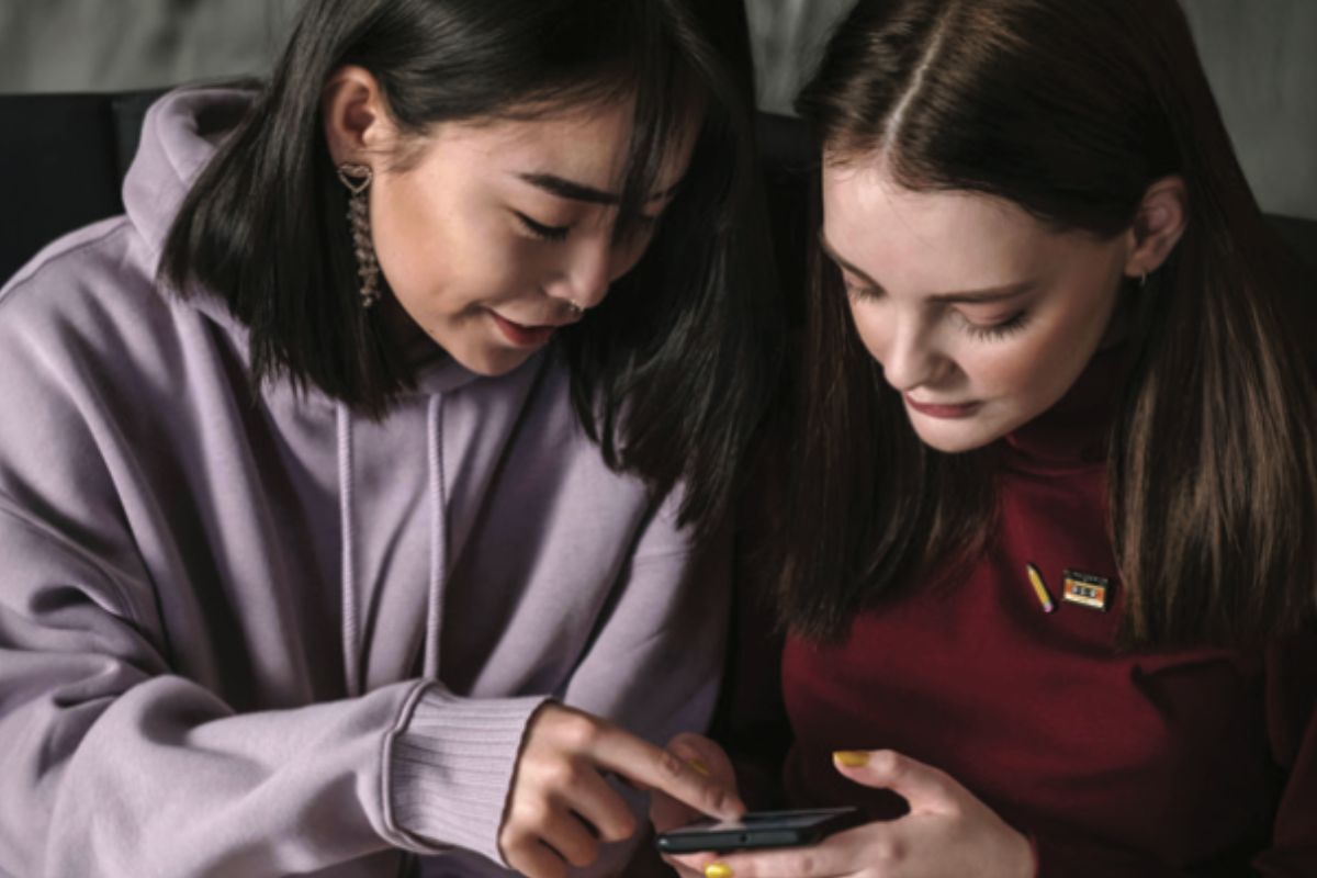 Two teenage girls huddle together to look on a phone.