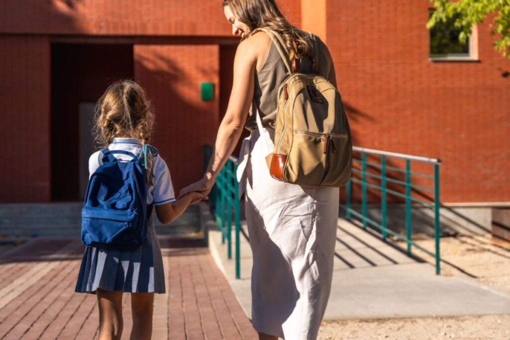 A mother and child walk hand in hand towards a school.