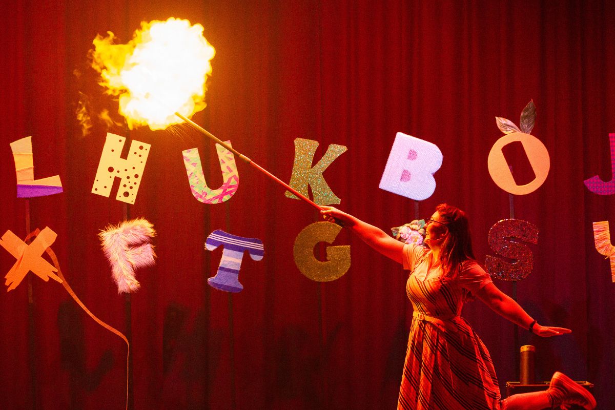 a woman performs with fire on a stage with letters of the alphabet engaging in an explosive performance