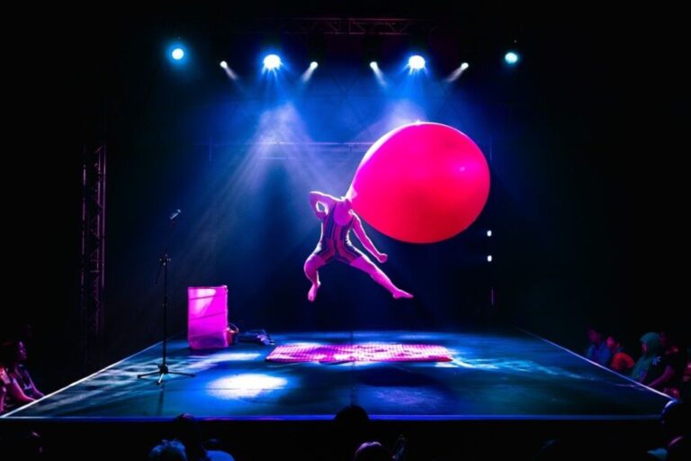 A man performs acrobatics on a stage with a giant balloon for a head.