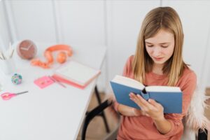 A girl reading a book at their desk in kids bedroom.
