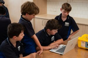 Four boys in school uniform work together around a laptop computer.