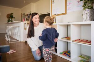 A woman and a child joyfully playing together in a colourful playroom filled with toys and soft furnishings.