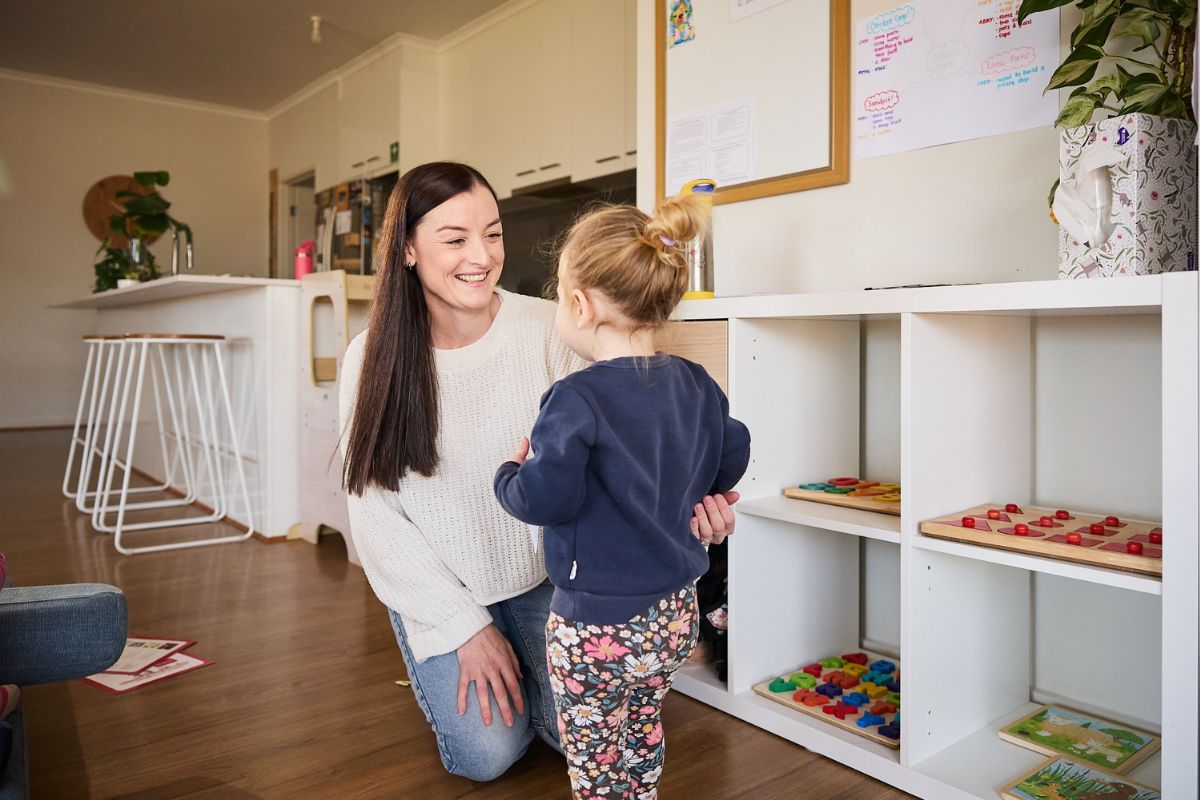 A woman and a child joyfully playing together in a colourful playroom filled with toys and soft furnishings.