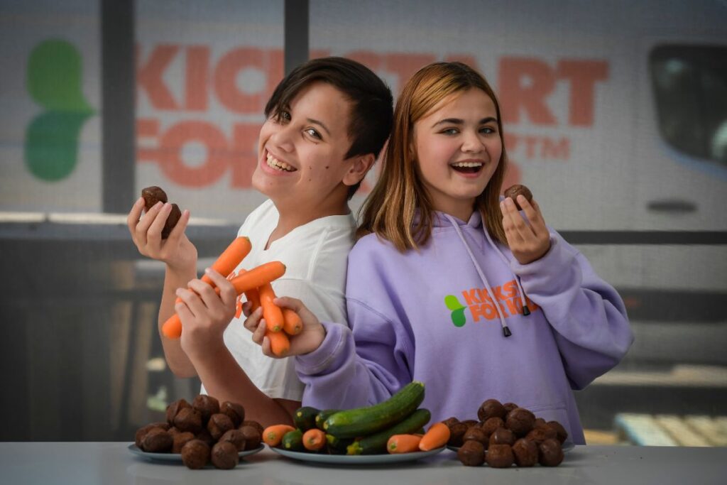 Two students posing with nutritious muffins and the ingredients used to make them including carrots.