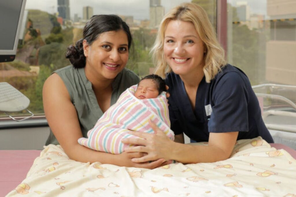 A midwife and patient with newborn baby smiling.