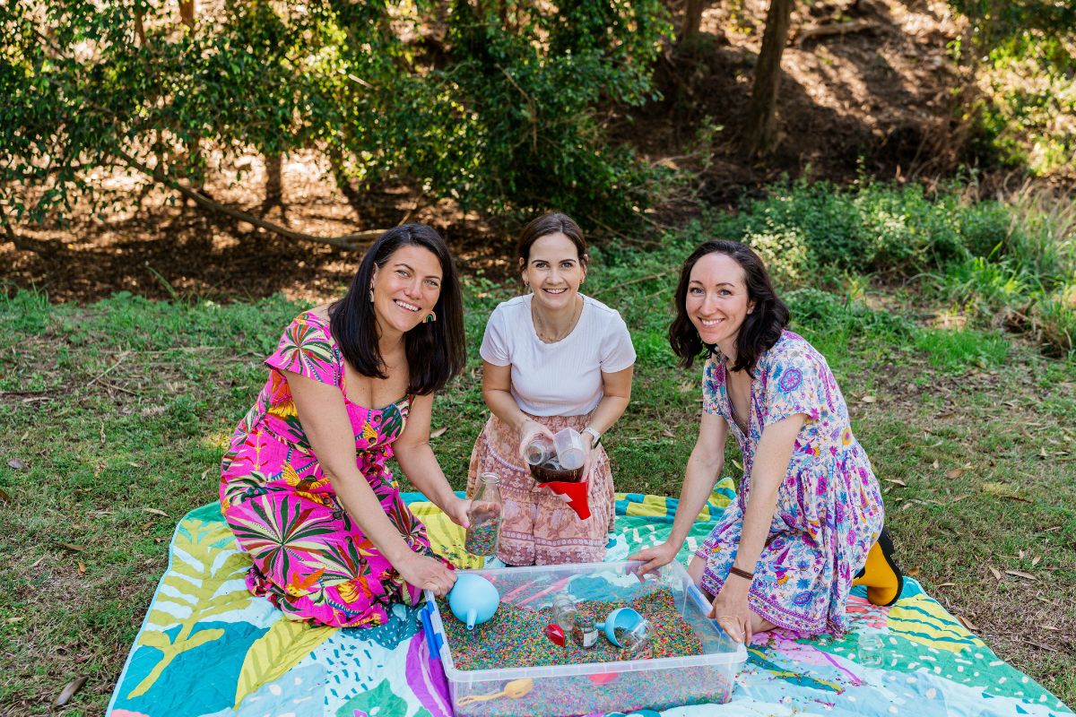 Play All Day App creators Emma Meyer, Gemma Rooke and Jacqui Burton sitting outside on a colourful blanket.