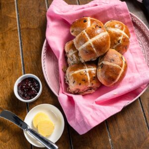 Hot cross buns on pink towel with butter and jam on the side.
