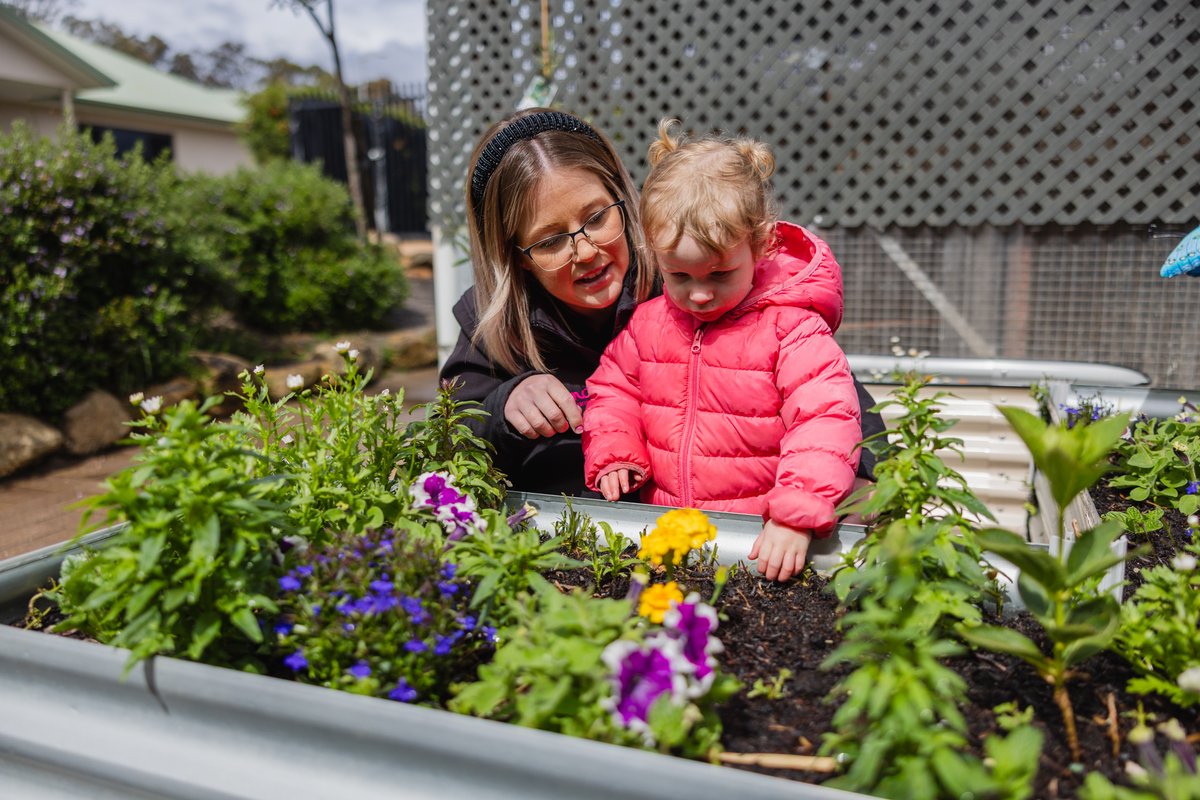 A childcare worker and small child playing in the garden of an Emali early learning centre.