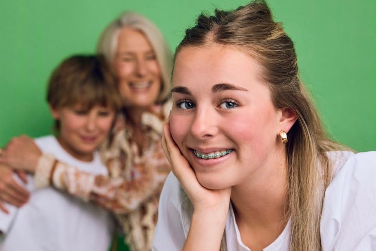A girl with braces smiling as her brother and parent look on.