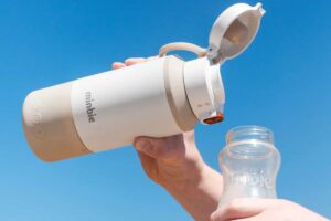 Minbie portable baby milk warmer and baby bottle on the go with blue sky in background.