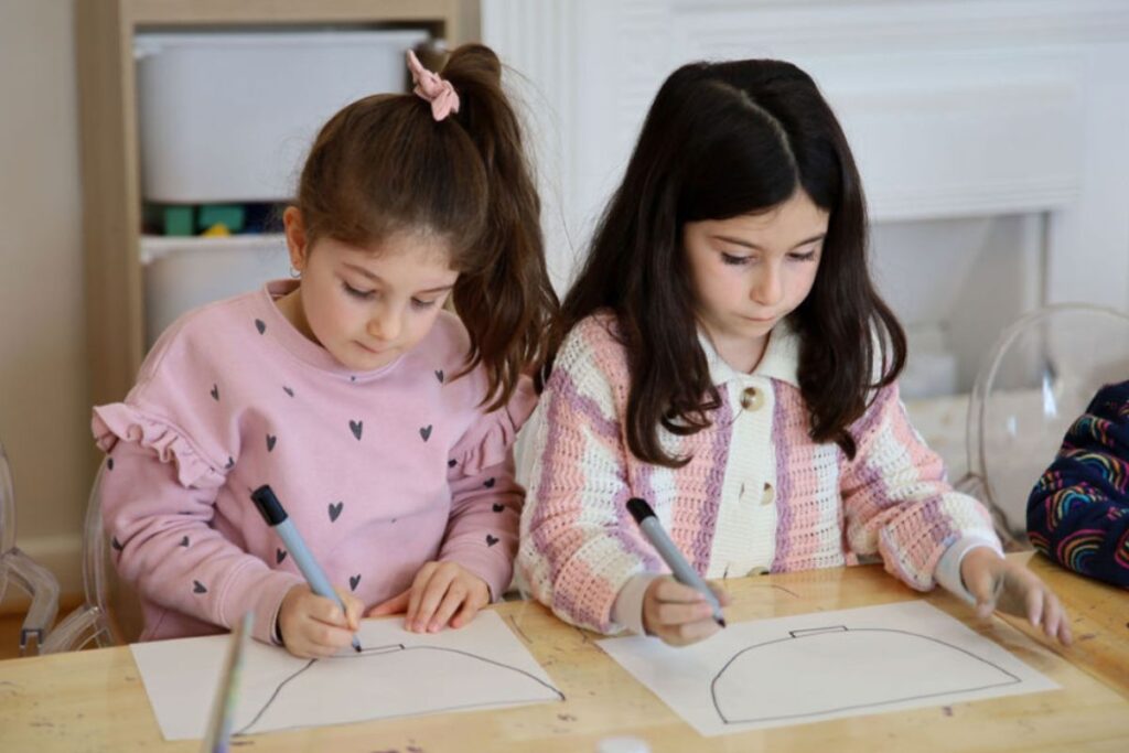 Two young girls dressed in pink focussed on an art drawing class.